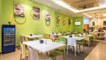 A restaurant with multiple tables and chairs, a beverage dispenser, and wall posters.