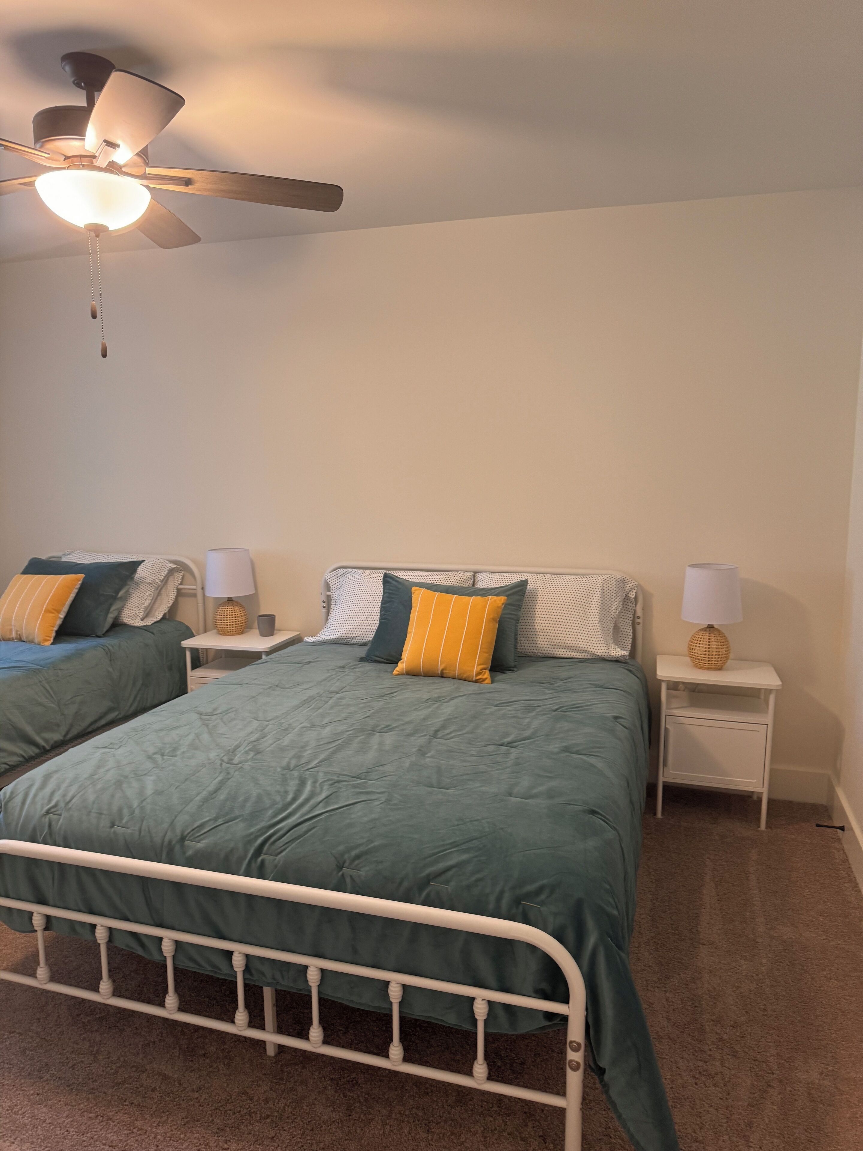 Ein Schlafzimmer mit zwei Betten, einem Deckenventilator, Nachttischlampen und einem Teppichboden.