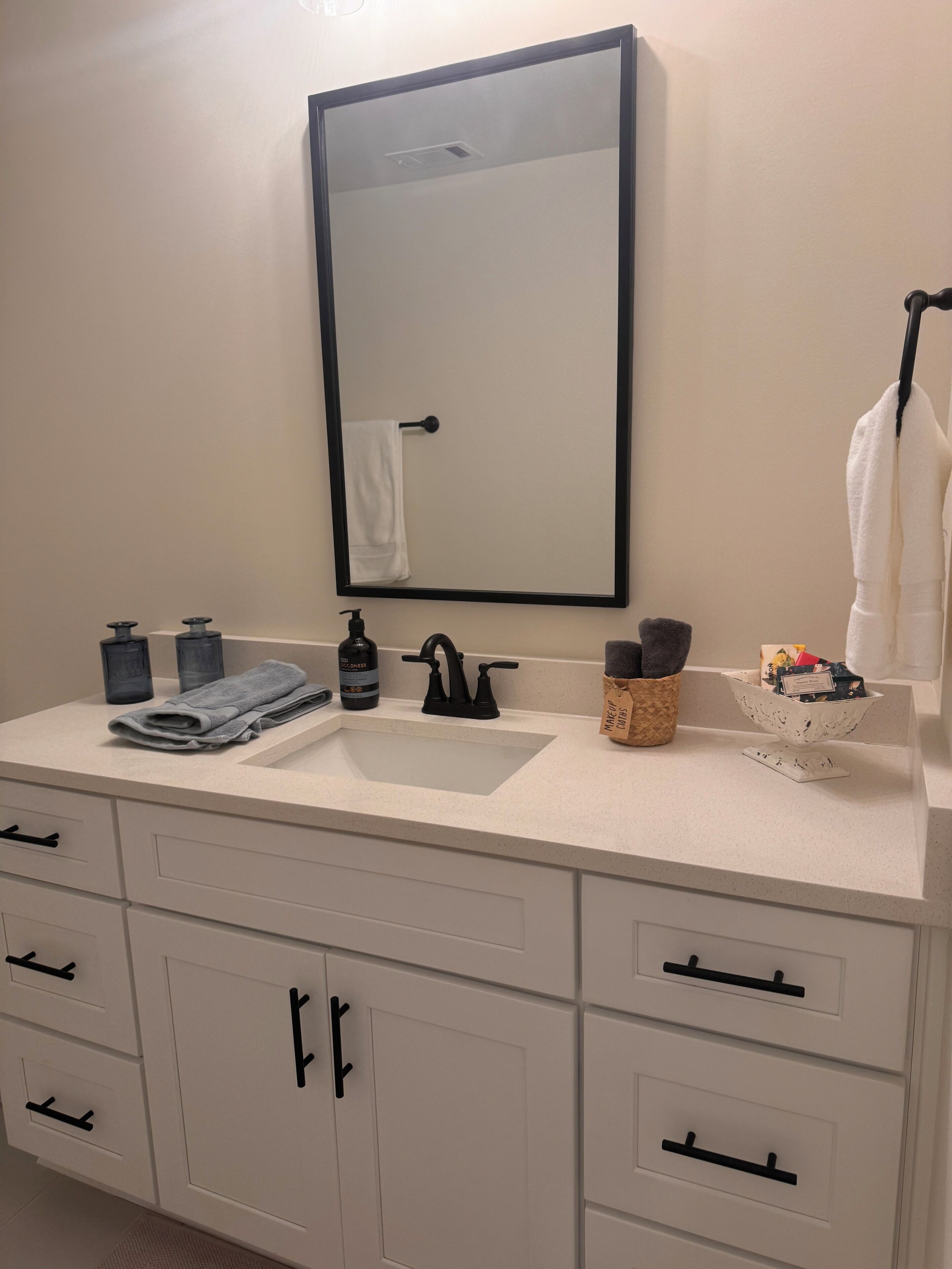 A bathroom with a white sink, black faucet, and a mirror above it. There are towels, a soap dispenser, and a small basket on the counter.