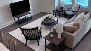 Een moderne woonkamer met een flatscreen televisie, een bank, een salontafel en een eethoek met stoelen.