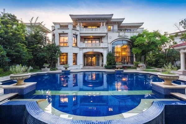 A large, multi-story house with a central pool and a well-maintained garden.