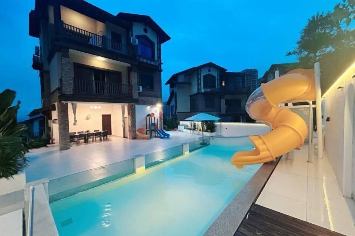 Une piscine avec un toboggan, un immeuble à plusieurs étages et un espace extérieur aménagé pour s’asseoir.