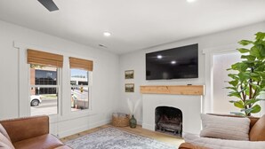 A living room with a fireplace, a television mounted on the wall, and a large window with blinds. - Charming 3 Bedroom Retreat: Perfect for Families, Travelers and Professionals (Billings)