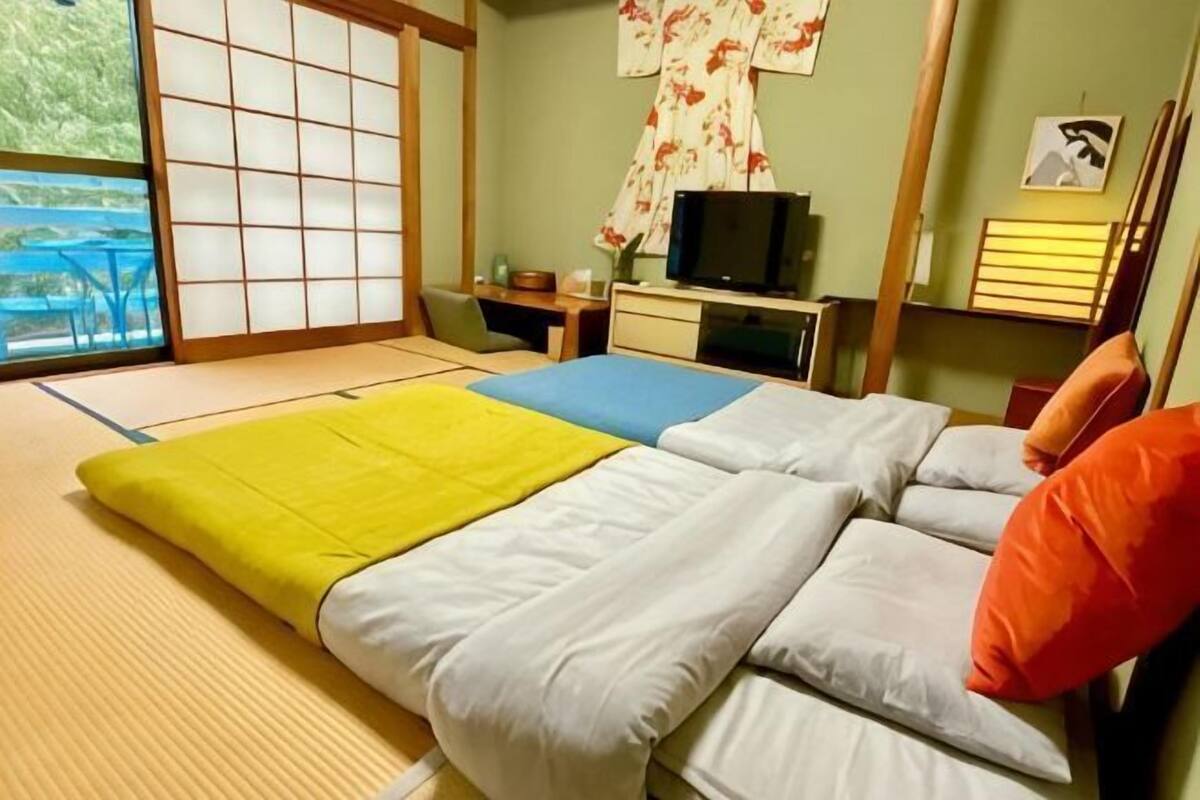 A room with tatami mats, a bed with pillows, a television, and a desk with a chair.