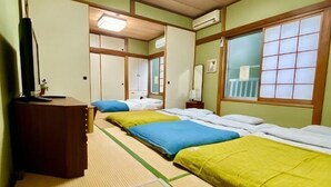 A room with tatami flooring, a desk, three beds with different colored bedding, a mirror, and a window with a grid pattern. - Hanamizuki Onsen Ryokan (Ito)