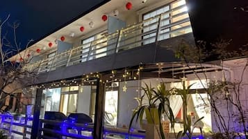Ein zweistöckiges Gebäude mit einem Balkon, Lichterketten und Blumentöpfen.