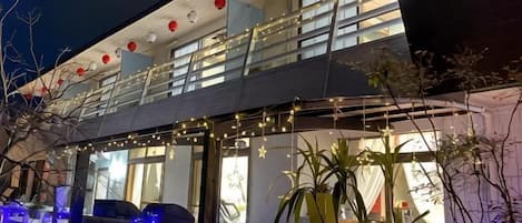 A two-story building with a balcony, string lights, and potted plants.