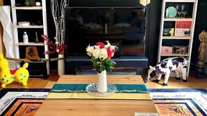 A living room with a TV, a wooden table, a vase with flowers, a yellow toy, and a cow statue. - Hanamizuki Onsen Ryokan (Ito)