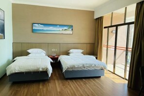 A hotel room with two beds, a painting of a beach scene, a nightstand, and a large window with curtains. - Changhong Business Hotel (Yangjiang)
