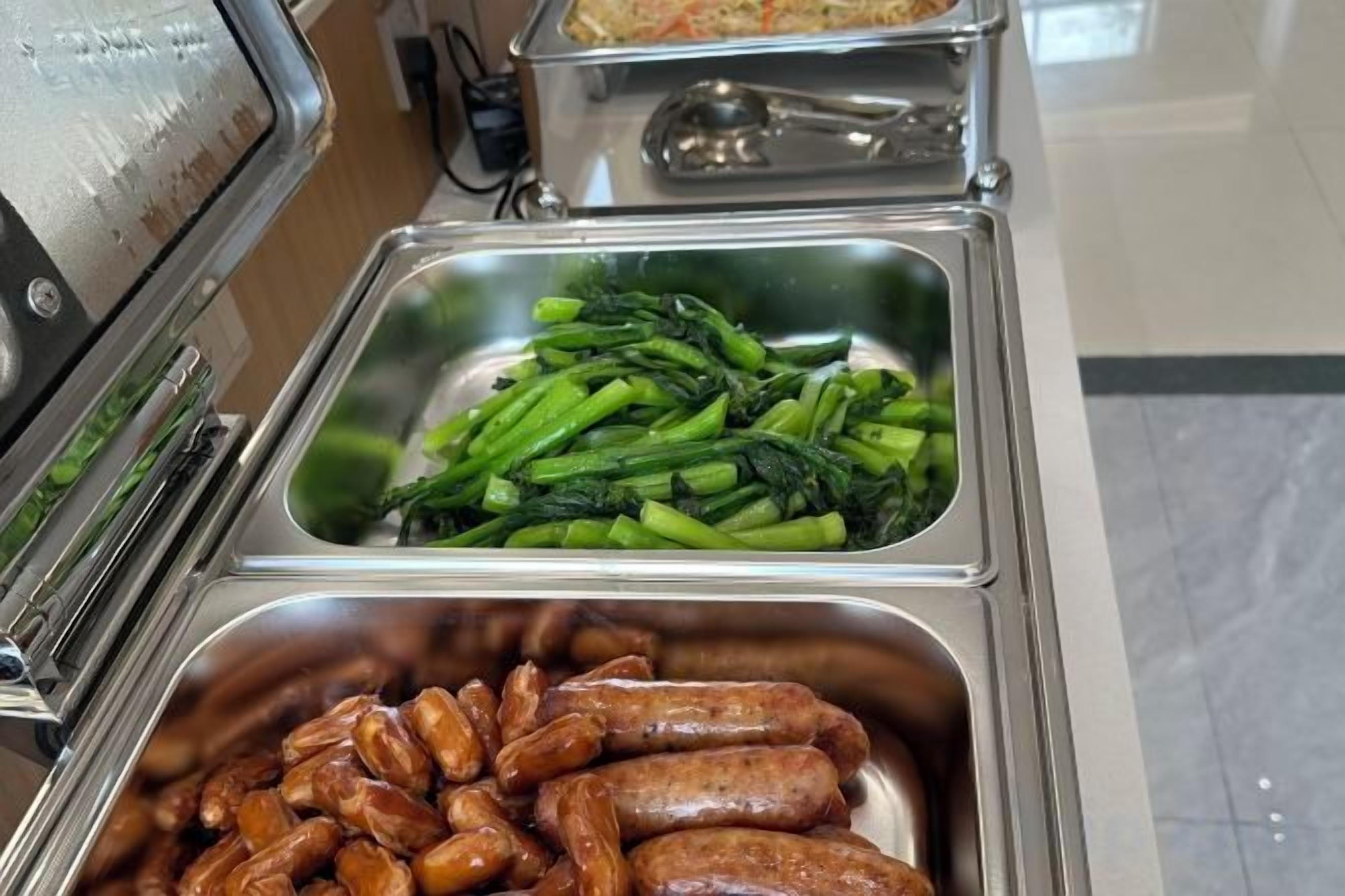 A buffet with various food options including sausages and green vegetables.