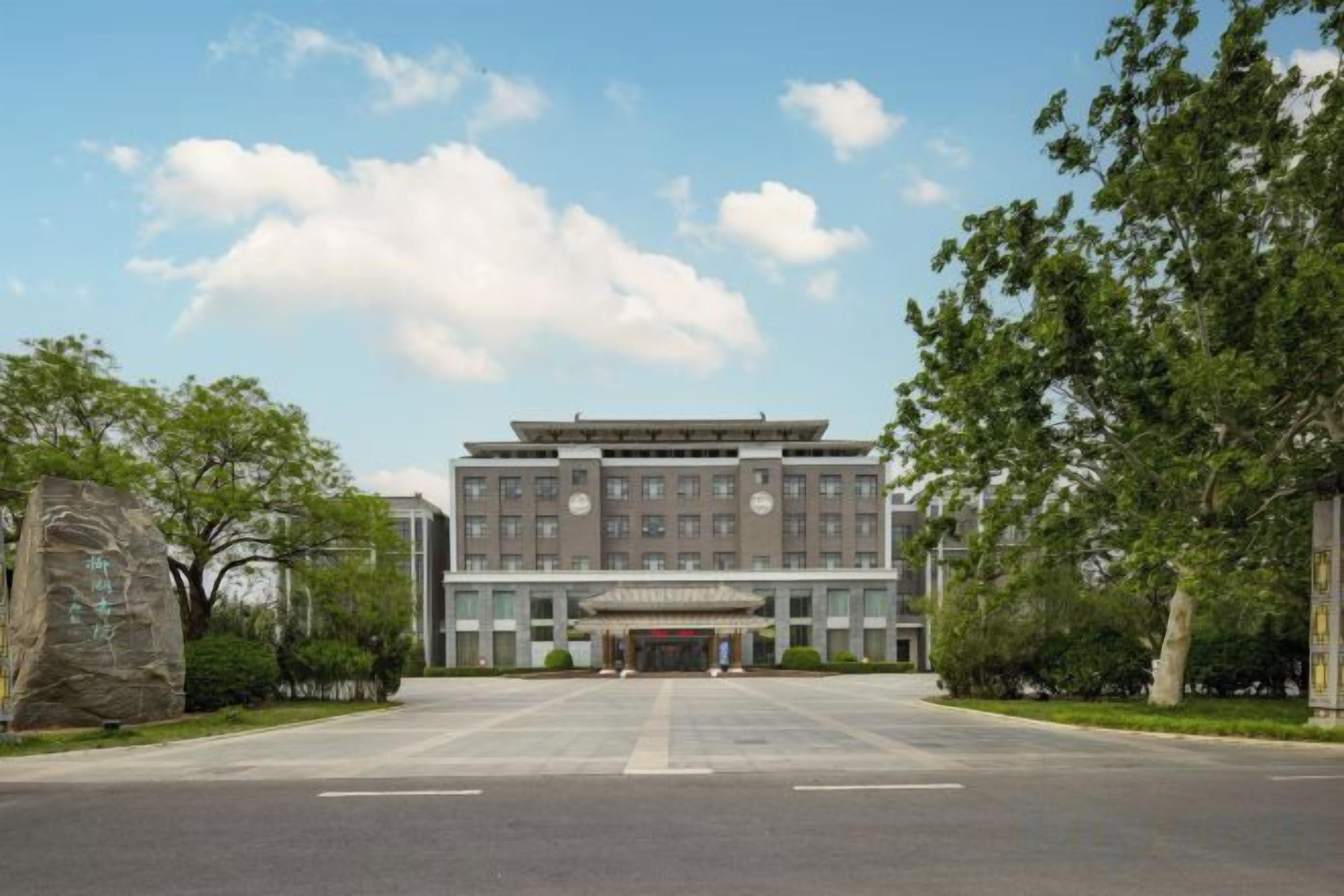 A large building with a central entrance, surrounded by trees and a paved area.