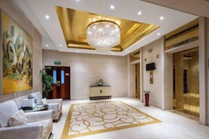 A hotel lobby with a chandelier, a reception desk, and a large painting on the wall.