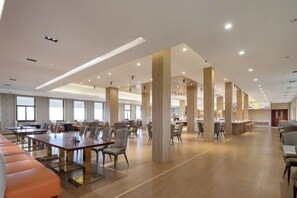 Une salle à manger d’hôtel spacieuse, dotée de nombreuses tables et chaises, de hauts plafonds et de grandes fenêtres.