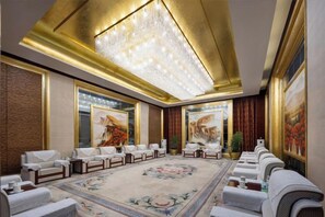 Une salle de conférence dotée d’un grand lustre, d’une moquette à motifs floraux et d’une rangée de canapés.