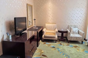 A room with a television on a wooden cabinet, two armchairs, a small table, and a patterned carpet. - Liuhu Hotel (Hot Spring Garden Hotel) (Dezhou)