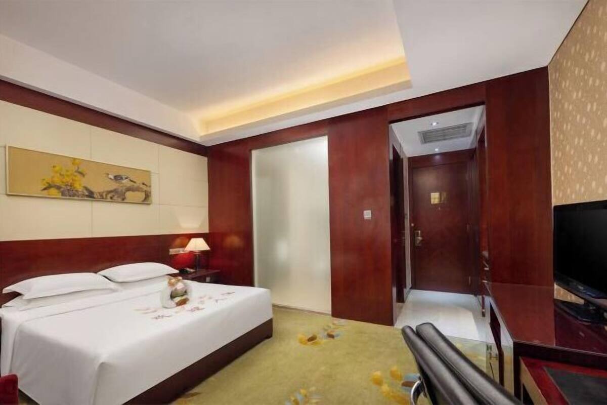Une chambre d’hôtel avec un lit, une télévision, un tableau au mur et une porte donnant sur une autre pièce.