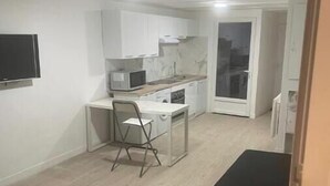 Une cuisine compacte avec des meubles blancs, un four à micro-ondes et un petit coin repas comprenant une chaise et une table.