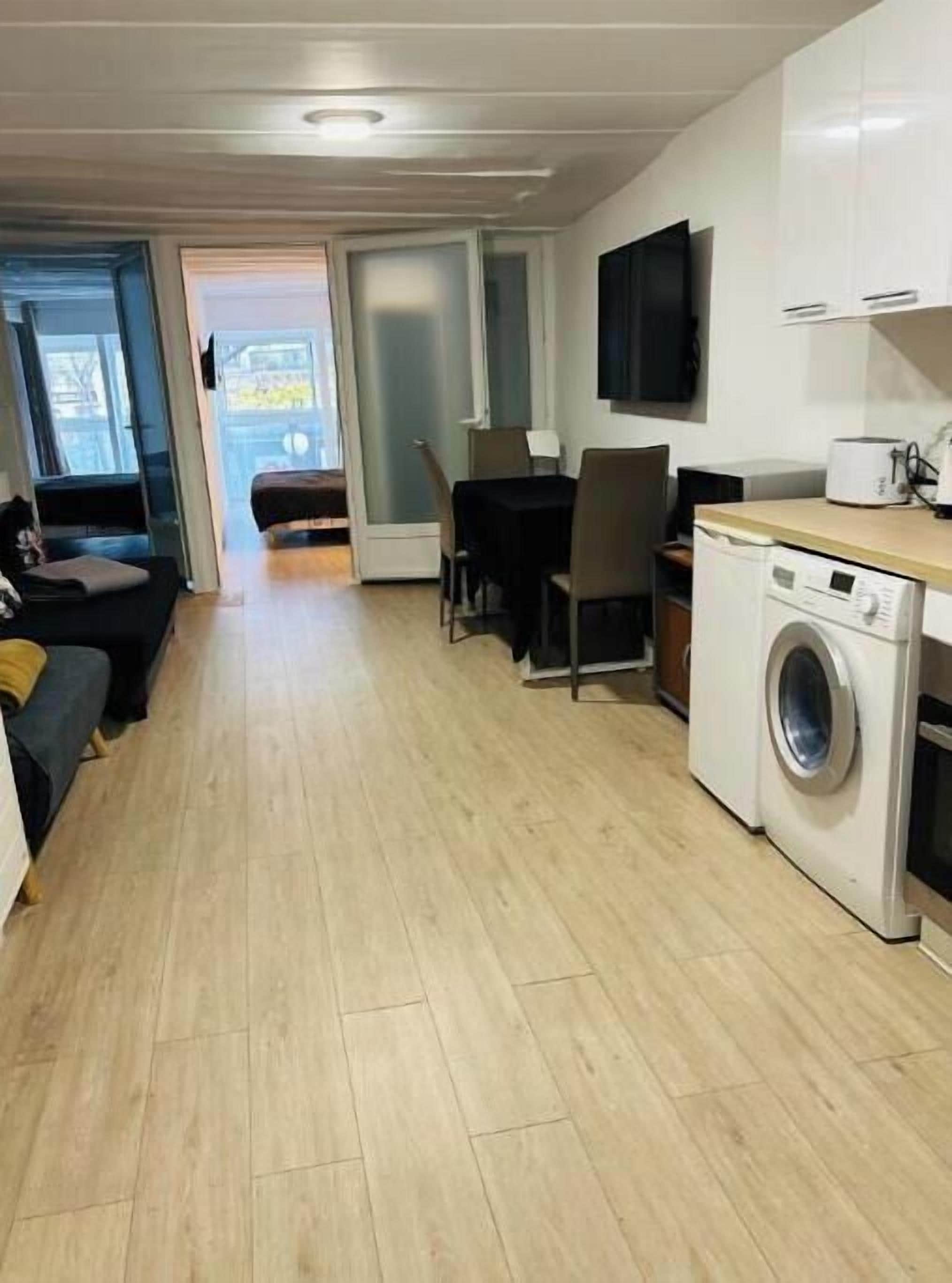 A compact living space with a dining area, a washing machine, and a TV mounted on the wall.