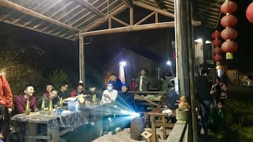 An outdoor gathering with a group of people around a table under a covered area.
