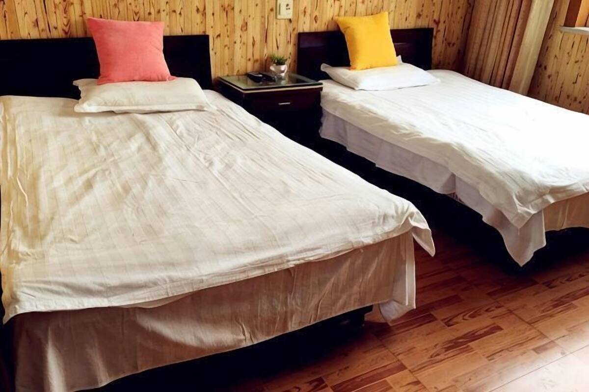 Deux lits simples avec du linge de lit blanc, une table de chevet avec une lampe et un plancher en bois.