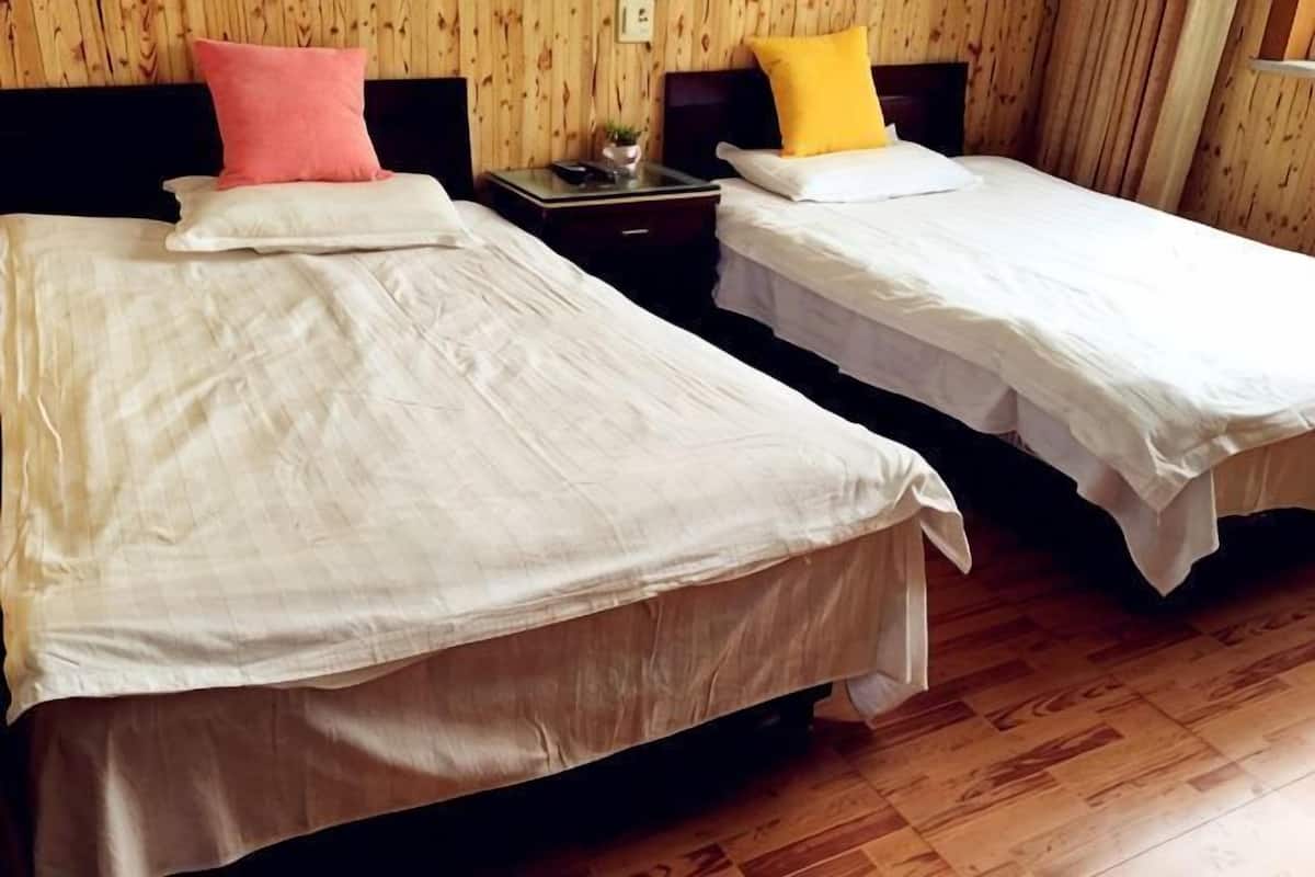 Two single beds with white linens, a nightstand with a lamp, and wooden flooring.