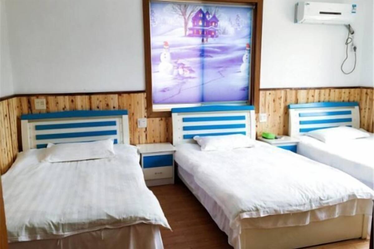 Une chambre avec deux lits, un lambris en bois, une fenêtre donnant sur une maison et un climatiseur fixé au mur.