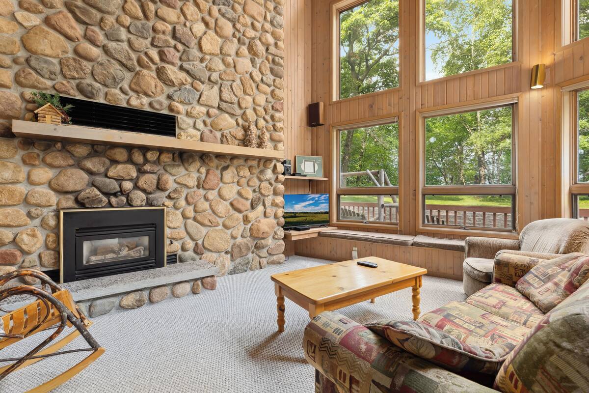 A cozy living room with a stone wall, fireplace, large windows, and comfortable seating.