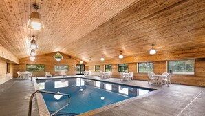 An indoor swimming pool with a wooden ceiling, surrounded by white chairs and tables. - Causeway on Gull (Nisswa)