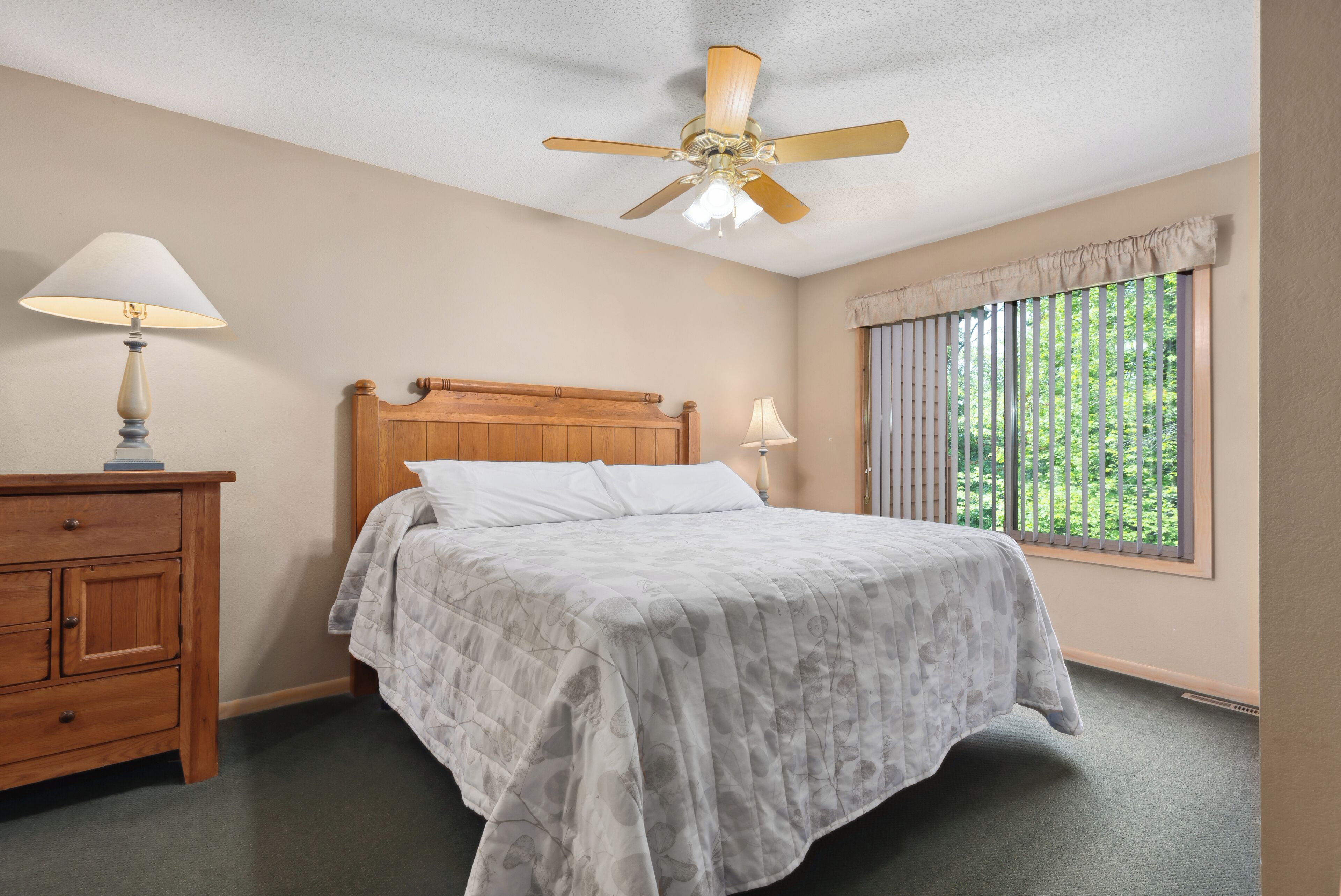 A bedroom with a wooden bed, a nightstand, a ceiling fan, and a window with blinds.