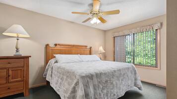 A bedroom with a wooden bed, a nightstand, a ceiling fan, and a window with blinds.