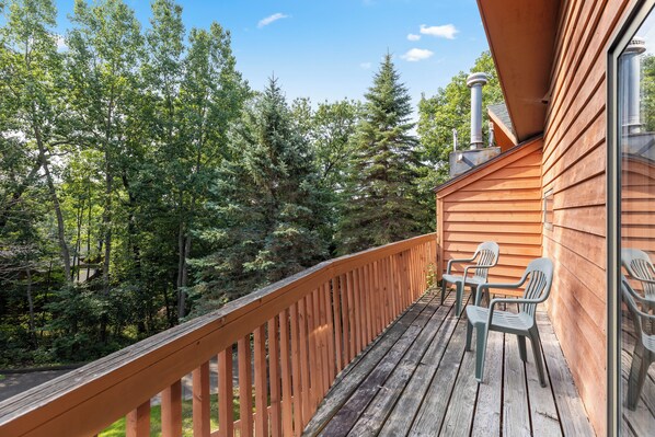 A wooden deck with a railing, two chairs, and a view of a forested area. - Causeway on Gull (Nisswa)