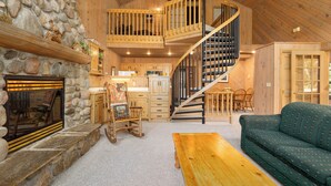 A spacious living area with a stone fireplace, wooden staircase, and a cozy green sofa. - Causeway on Gull (Nisswa)