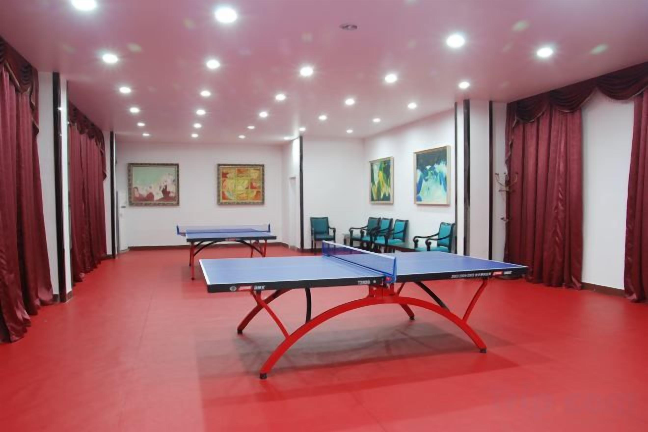 Una habitación con dos mesas de ping pong, cortinas rojas y obras de arte en las paredes.