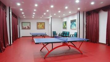 Una habitación con dos mesas de ping pong, cortinas rojas y obras de arte en las paredes.