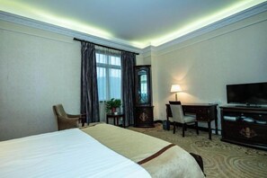 A hotel room with a bed, a desk, a chair, a television, and a lamp. - Huchuan Hotel (Yueqing)