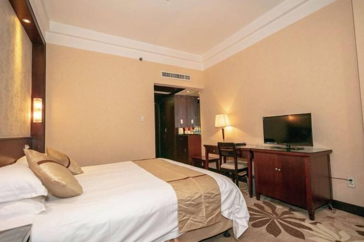 Quarto de hotel com cama, escrivaninha, televisão e armário.