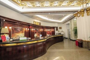 A reception desk with a curved design, framed artwork above, and a clock on the wall. - Huchuan Hotel (Yueqing)