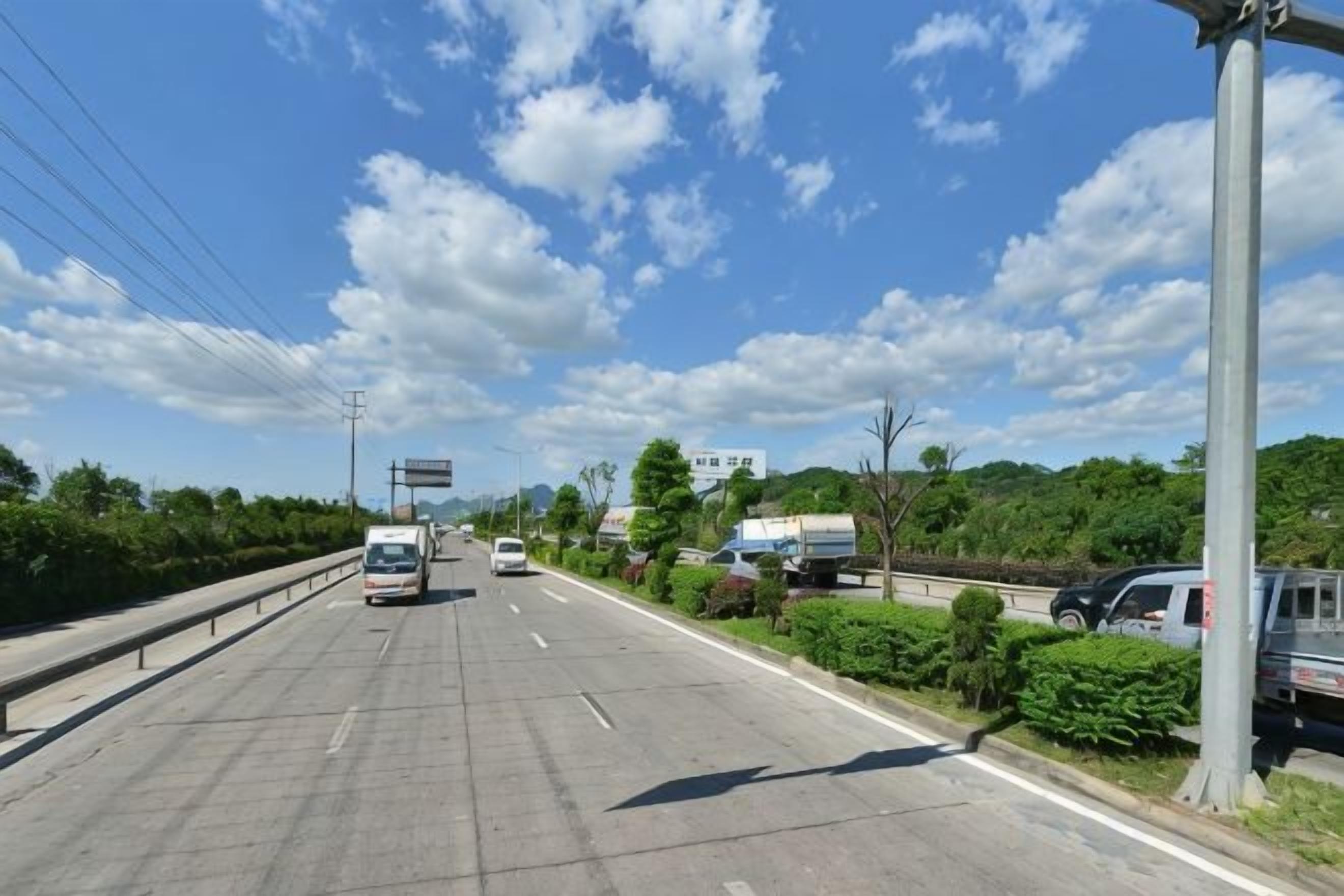 Motorvej med flere vognbaner, biler, grønt langs vejen og en klar himmel.