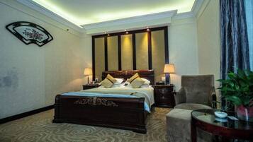 Quarto de hotel com uma cama grande, duas mesas de cabeceira com luminárias, uma cadeira e uma pequena mesa com uma planta.