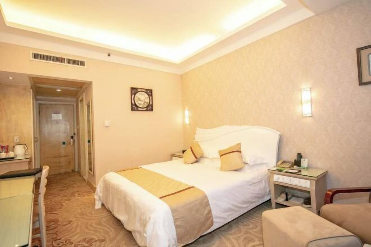 Quarto de hotel com cama, mesa de cabeceira, poltrona e escrivaninha com cadeira.