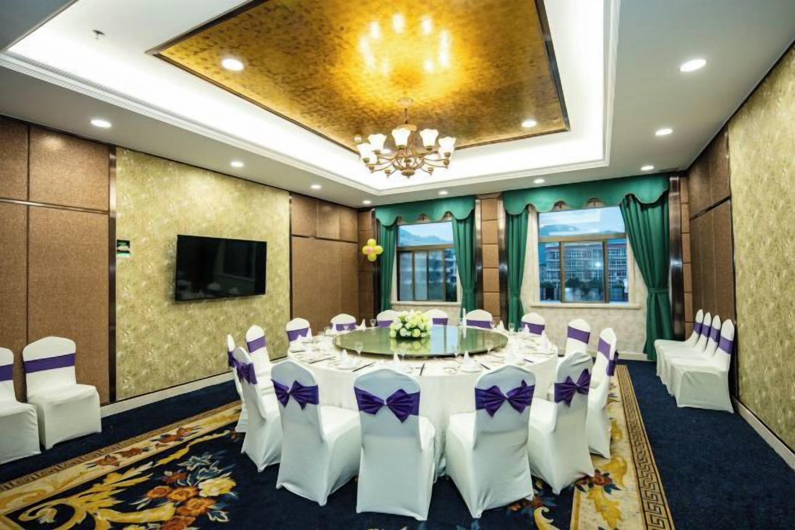 A conference room with a round table, white chairs with purple sashes, a chandelier, a flat-screen TV, and a city view through the windows.