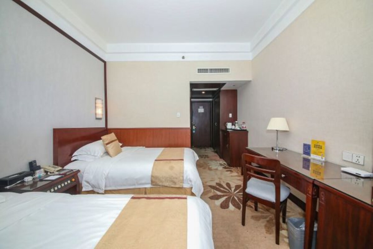 A hotel room with two beds, a desk, a chair, and a small table.
