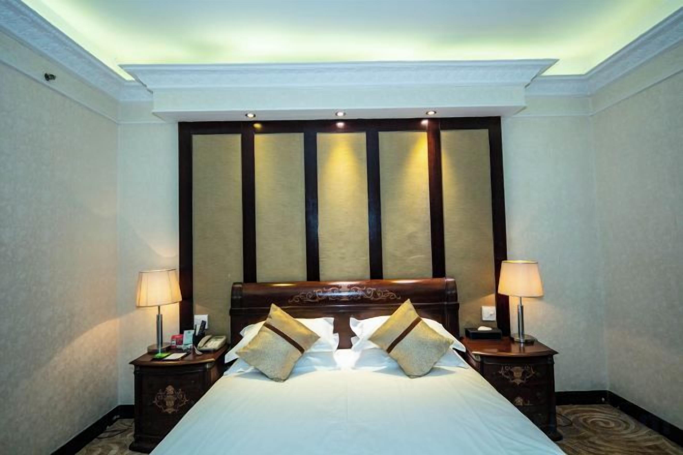 Una habitación de hotel con una cama grande, dos mesitas de noche y un cabecero con paneles verticales.