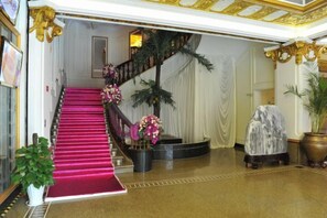 A grand staircase with a red carpet leading to a landing area, surrounded by potted plants and a large covered seating area. - Huchuan Hotel (Yueqing)