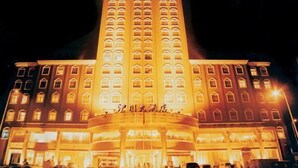Un hotel con una entrada central destacada, varios pisos y ventanas iluminadas.