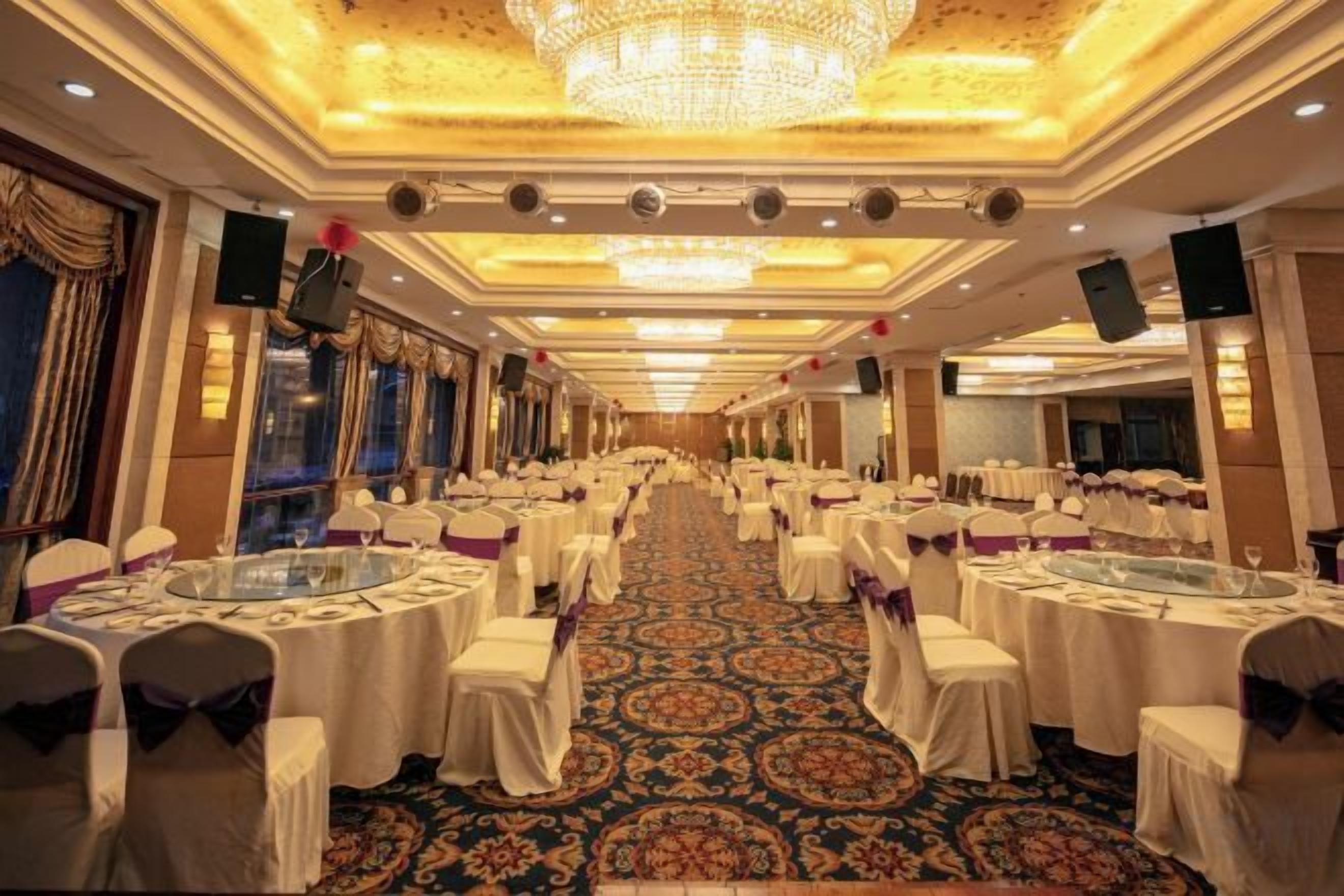 Un salón de banquetes con mesas redondas, sillas y una alfombra estampada.