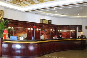 A reception desk with a curved design, a framed picture above it, and a red lamp to the left. - Huchuan Hotel (Yueqing)