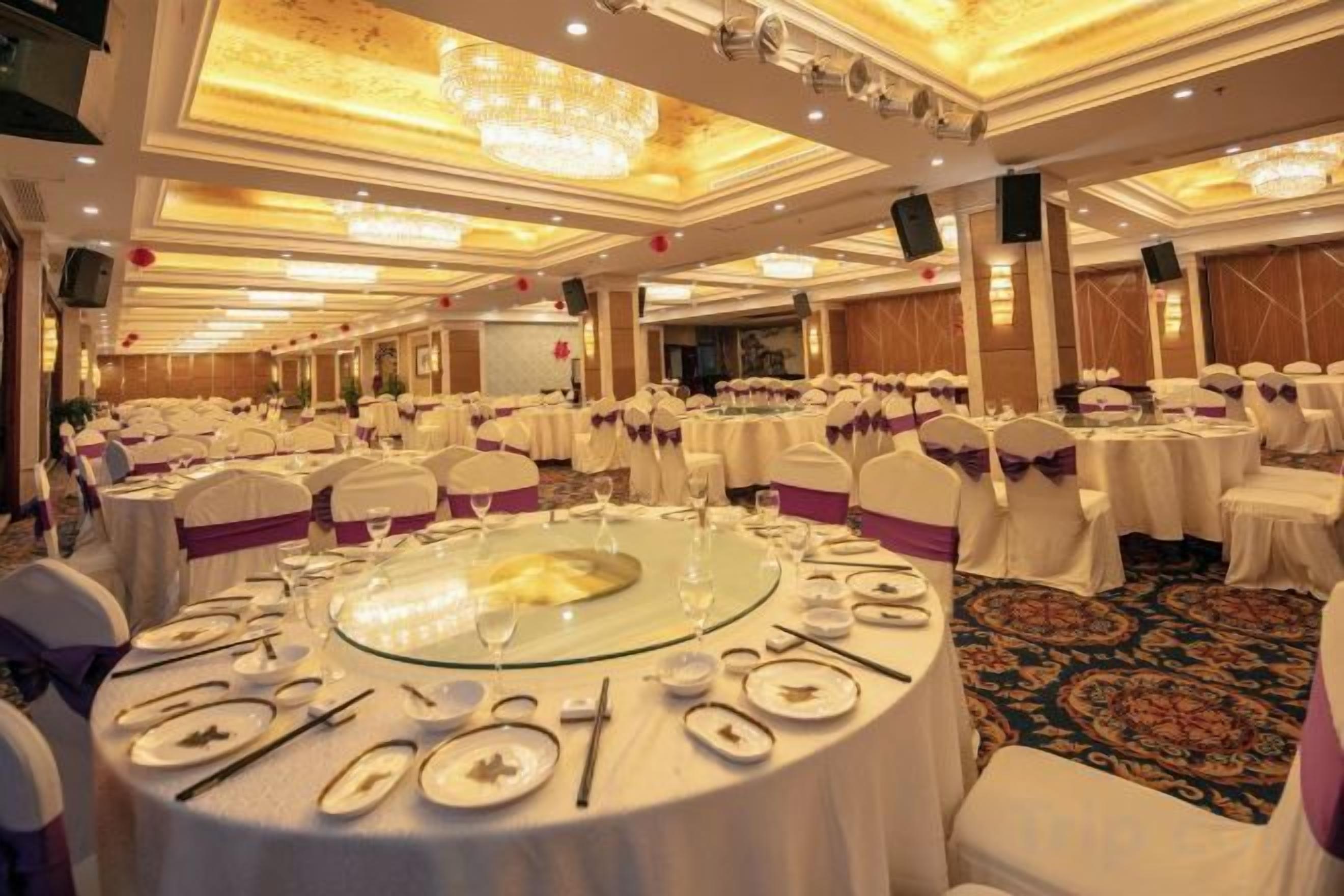 A banquet hall with round tables set for a formal event, featuring a central floral arrangement.