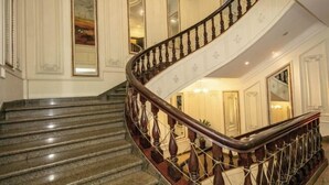 Una imponente escalera de madera con barandilla y balaustradas, que conduce a un rellano con candelabro.