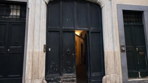 Une façade d’immeuble avec une entrée centrale, flanquée de deux fenêtres avec volets, et un arc décoratif au-dessus des portes.